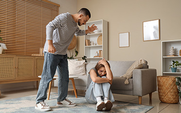 Man standing over cowering woman; protecting rights against false domestic violence allegations.
